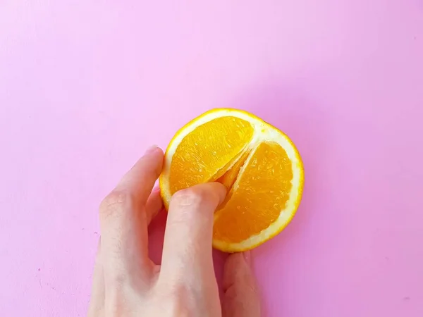 A vagina symbol. The concept of sex. Finger on an orange on a pink background. — Stockfoto