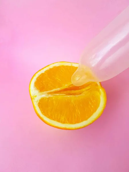 The concept of safe sex and protection. A vagina symbol. A juicy orange and a condom on a bright pink background. — Stock Photo, Image