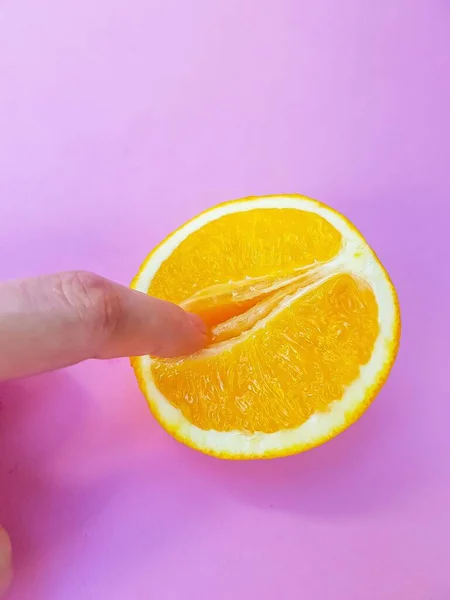 A vagina symbol. The concept of sex. Finger on an orange on a pink background. — Stock Photo, Image