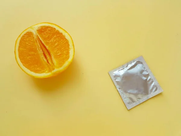 The concept of safe sex and protection. A vagina symbol. A juicy orange and a condom on a bright yellow background. ストックフォト