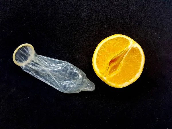 O conceito de sexo seguro e proteção. Um símbolo da vagina. Uma laranja suculenta e um preservativo em um fundo preto . — Fotografia de Stock