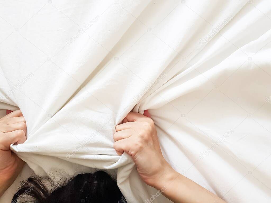 Close up sexy woman hand pulling and squeezing white sheets in ecstasy in bed. Orgasm on white bed. Sex and erotic concept.