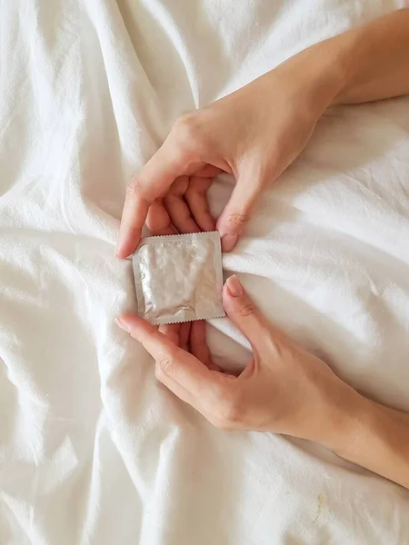 Fecha. Uma menina segura um preservativo em uma mão em uma cama branca. O conceito de sexo e erotismo . — Fotografia de Stock