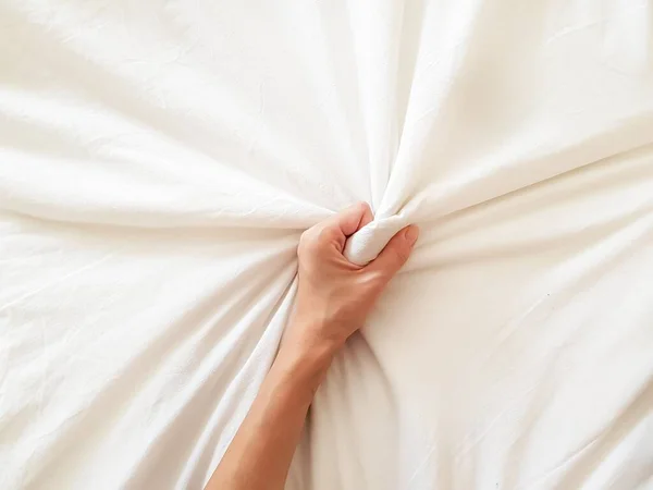 Κοντινό πλάνο σέξι γυναίκα χέρι τραβώντας και πιέζοντας λευκά σεντόνια σε έκσταση στο κρεβάτι. Οργασμός στο λευκό κρεβάτι. Σεξ και ερωτική έννοια. — Φωτογραφία Αρχείου