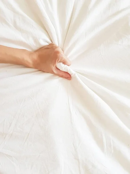 セクシーな女性の手を閉じてベッドの中でエクスタシーで白いシートを引っ張ると絞る。白いベッドの上のオーガズム。セックスとエロティックなコンセプト. ストック画像