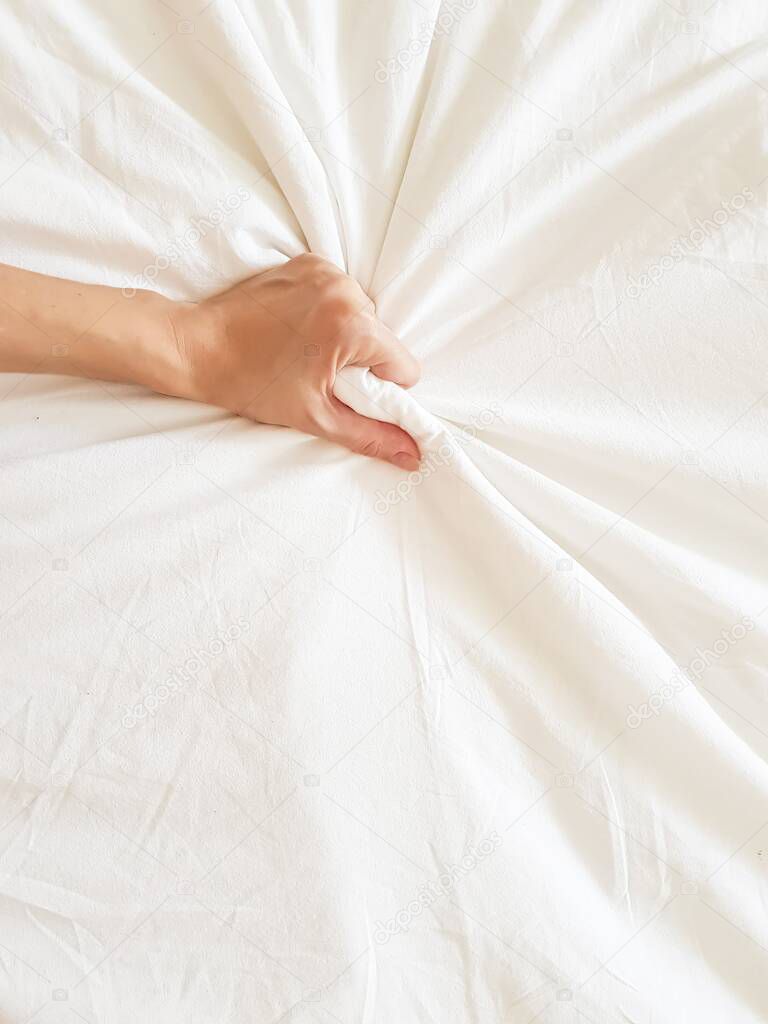 Close up sexy woman hand pulling and squeezing white sheets in ecstasy in bed. Orgasm on white bed. Sex and erotic concept.