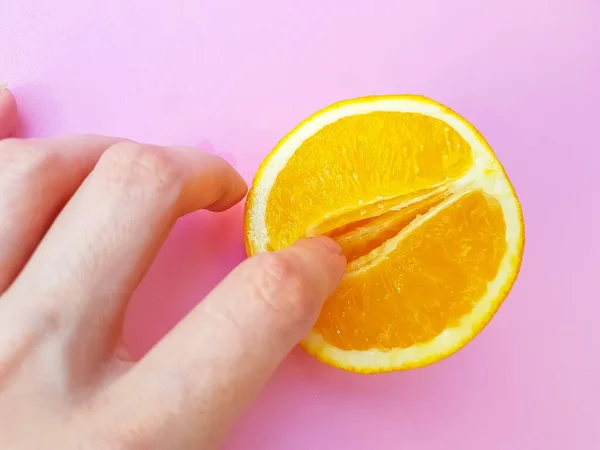 A vagina symbol. The concept of sex. Finger on an orange on a pink background. — Stock Photo, Image