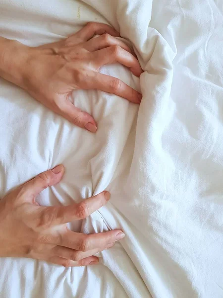 Nahaufnahme sexy Frau Hand zieht und quetscht weiße Laken in Ekstase im Bett. Orgasmus auf weißem Bett. Sex und erotisches Konzept. — Stockfoto