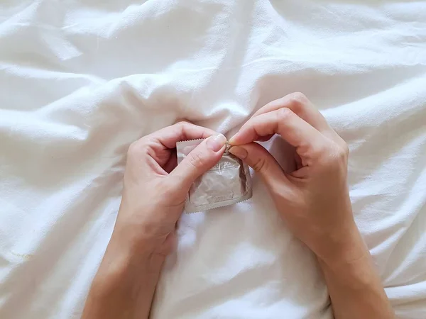 Fecha. Uma menina segura um preservativo em uma mão em uma cama branca. O conceito de sexo e erotismo . — Fotografia de Stock