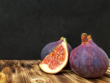 Koyu bir arka planda, ahşap yüzeyde parlak olgun incirler..