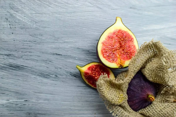 Leuchtend violette üppige Feigen wickeln sich in Stoff auf grauem Holzhintergrund. — Stockfoto