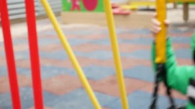 Yeşil ceketli şirin bir çocuk parkta sallanıyor.