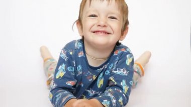 Sevimli küçük bir çocuk beyaz bir yüzeye uzanmış gülümsüyor ve ayağa kalkıyor