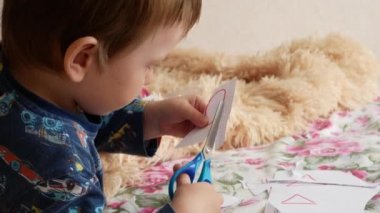 Küçük bir çocuk kağıt geometrik figürü dikkatlice makasla kesiyor.