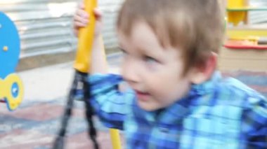 Ekose gömlek giymiş, çocuk parkında sallanan sevimli küçük bir çocuğun yakın çekimi.