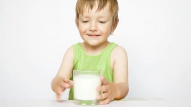 Küçük tatlı bir çocuk beyaz arka planda bir bardaktan süt içiyor.