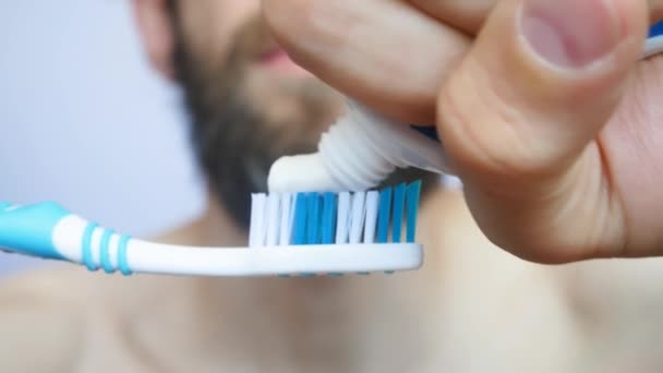一个留着胡子的年轻人把牙膏压在刷子上刷牙 — 图库视频影像