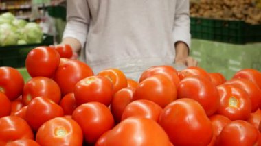 Genç bir kadın markette olgun domatesleri dikkatlice topluyor.