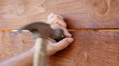 Bir adamın elleri ahşap bir duvara çivi çakıyor.