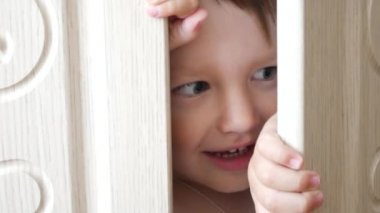 Küçük sevimli bir çocuk beyaz bir dolapta saklanırken eğleniyor.