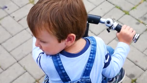 Ένα Μικρό Αγόρι Οδηγεί Ένα Μικρό Ποδήλατο Ένα Δρόμο Κοιτάζοντας — Αρχείο Βίντεο