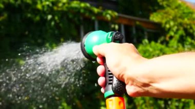 Sulama spreyi tutan ve bahçedeki bitkileri sulayan bir adamın elini kapat.