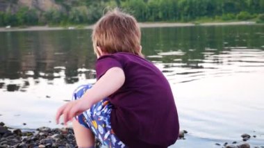 Küçük bir çocuk nehir kıyısındaki suya taş attı.