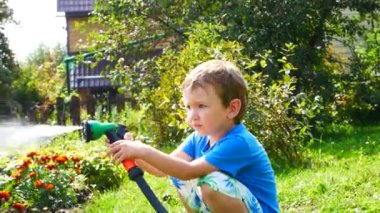 Küçük bir çocuk bahçedeki çiçekleri sulandıran bir spreyle sulıyor.