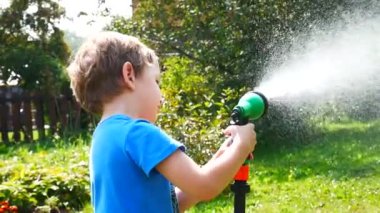Küçük bir çocuk sulama spreyiyle yeşil çimleri sular.