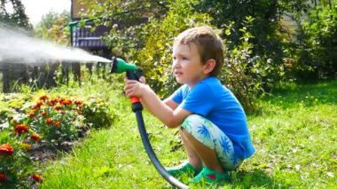 Küçük bir çocuk bahçedeki çiçekleri sulandıran bir spreyle sulıyor.