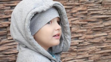 Kapüşonlu, kocaman bir yelek giymiş sevimli, gülümseyen bir çocuk.