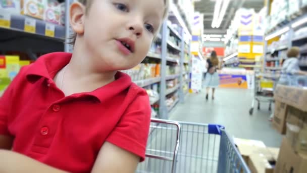 Крупный План Милого Мальчика Сидящего Корзине Между Полками Супермаркета — стоковое видео