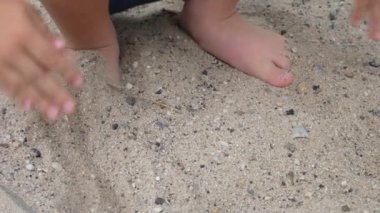 Küçük bir çocuk ayaklarını kuma gömüyor.