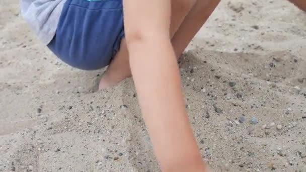 Menino Enterra Seus Pés Areia Agachando Salta Para Fora Dela — Vídeo de Stock