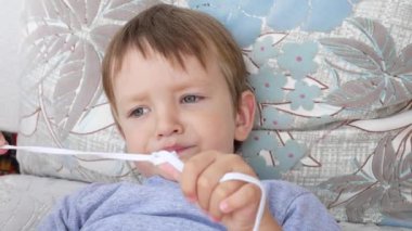 Sevimli bir çocuk kanepede uzanıyor, dinleniyor ve beyaz bir dantelle yakından oynuyor.