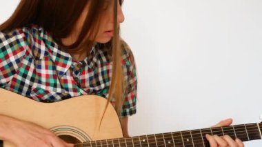 Renkli kareli gömlek giymiş genç bir bayanın yakın plan beyaz arka planda akustik gitar çalması