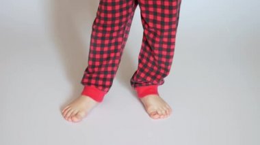 Kırmızı ekose pantolon giyen küçük bir çocuk ayağını beyaz zemine basıyor.