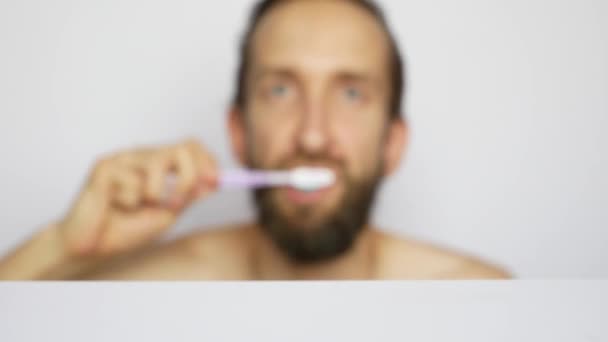 一个留着胡子的年轻人从架子上拿起牙刷刷牙 — 图库视频影像