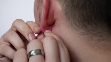 Genç bir adam kulağından küpe çıkarıyor. Yakından.