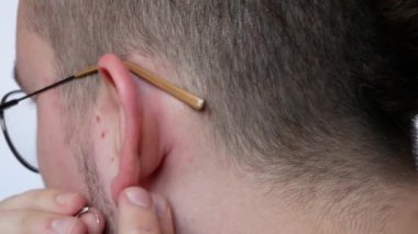 Gözlüklü yakışıklı bir adam kulağına küpe takıyor.