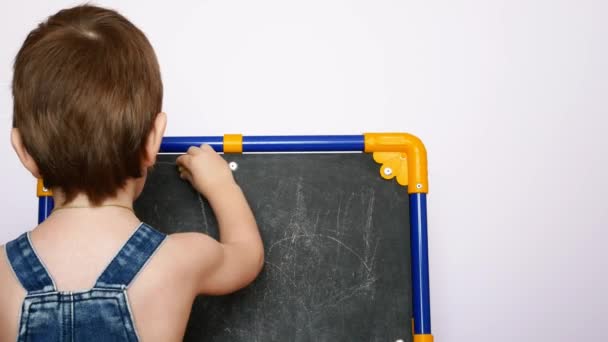 Ein Kleiner Junge Jeanshose Zeichnet Mit Kreide Auf Eine Tafel — Stockvideo