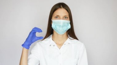 Koruyucu maskeli genç ve güzel bir hemşire uluslararası dilde sağır anlamına gelen COVID-19 kelimesinin işaretlerini gösteriyor.