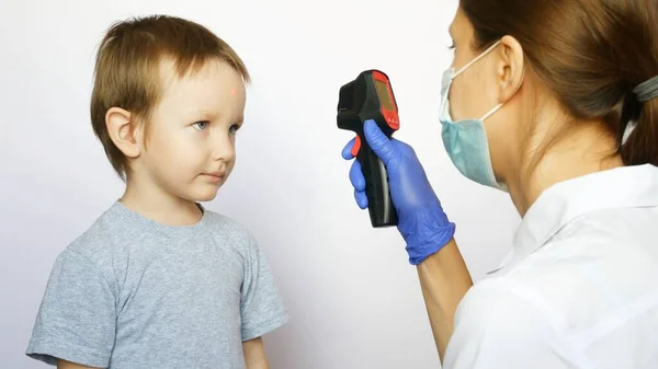 Bir kadın doktor, dijital termometre kullanan küçük bir çocuğun ısısını ölçer.