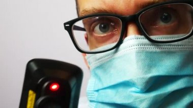 Koruyucu yüz maskesi ve gözlüklü bir doktor dijital termometre kullanan bir hastanın ısısını ölçer.