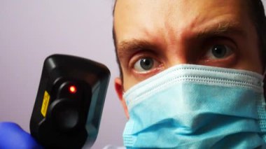 Koruyucu yüz maskesi olan bir doktor dijital termometre kullanan bir hastanın ısısını ölçer.