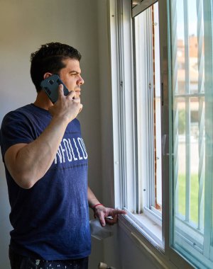Pencerenin yanındaki odada cep telefonuyla konuşan bir adam.