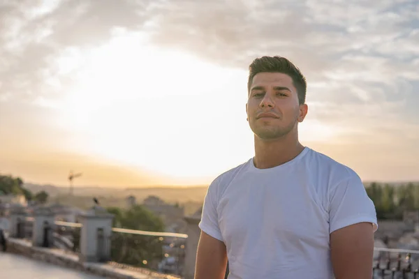 Beyaz tişörtlü, kahverengi saçlı, arka planda gökyüzü olan çocuk.