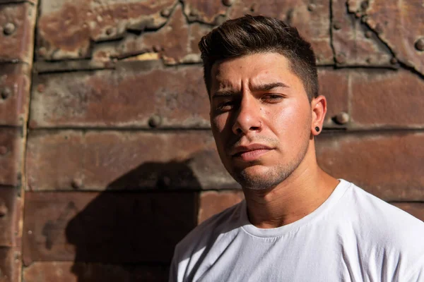 Paslı arka planı, beyaz tişörtü ve siyah küpesi olan bir adam.