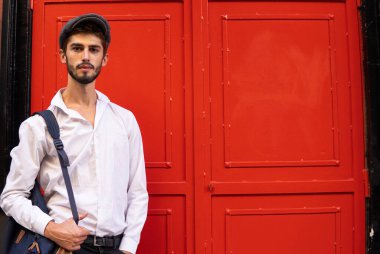 Kırmızı kapının önünde bereli ve sırt çantalı genç bir çocuk.