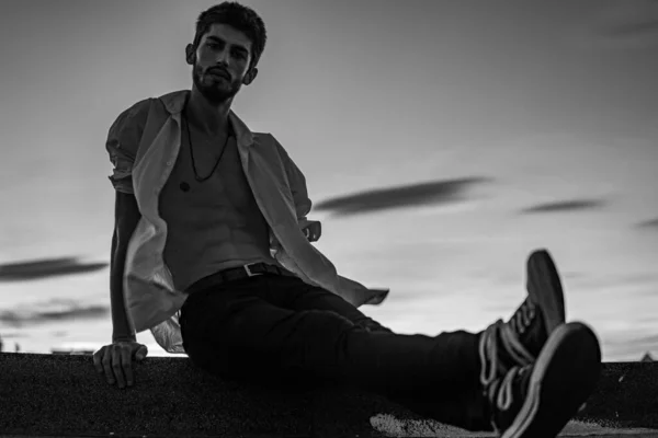 Eşcinsel çocuk beyaz bir tişörtle çatıda poz veriyor düğmeleri açık ve anın tadını çıkarıyor.